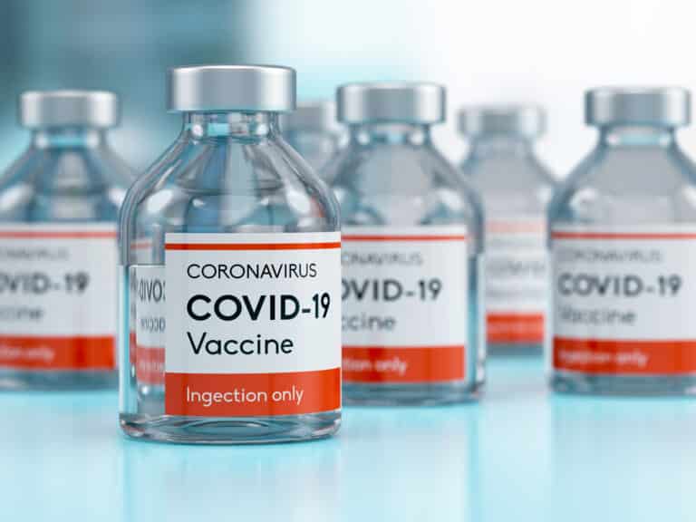 Vials labeled COVID-19 Vaccine lined up on a light blue surface
