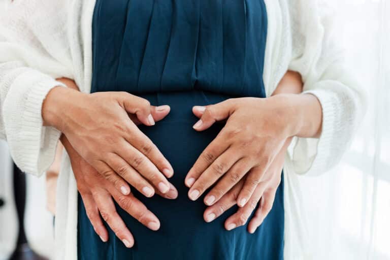 Couple’s hands resting together on a pregnant belly