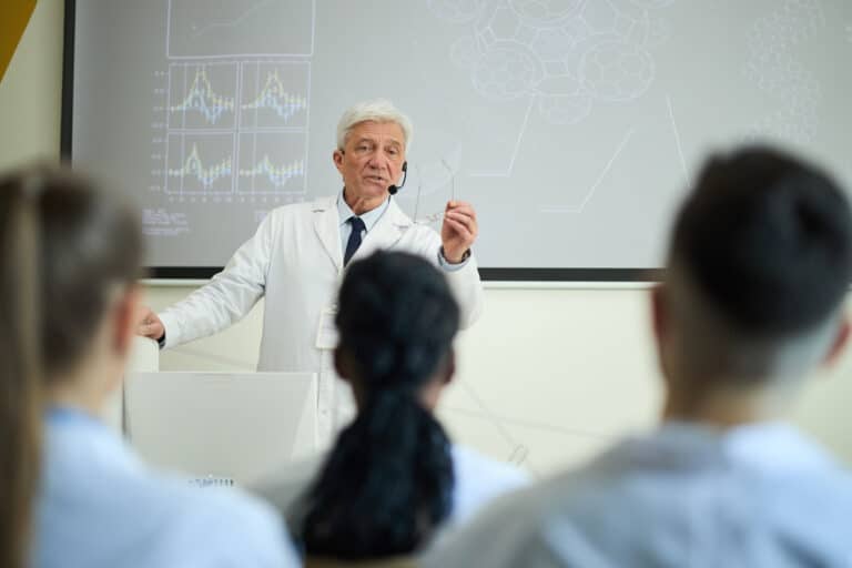 Senior doctor in a white coat lecturing a classroom of students