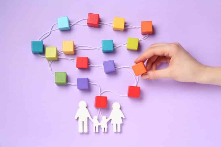 Hand arranging colorful cubes into a family tree above white family figures on a lilac background
