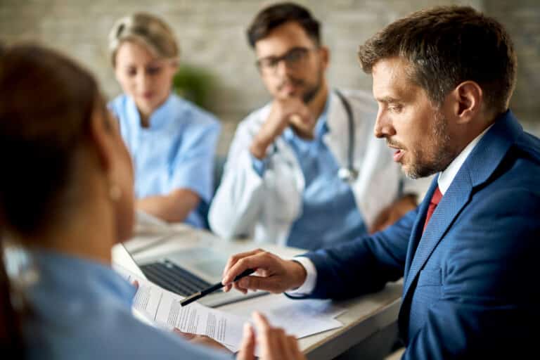 Man in a suit reviewing documents with doctors at a table with a laptop