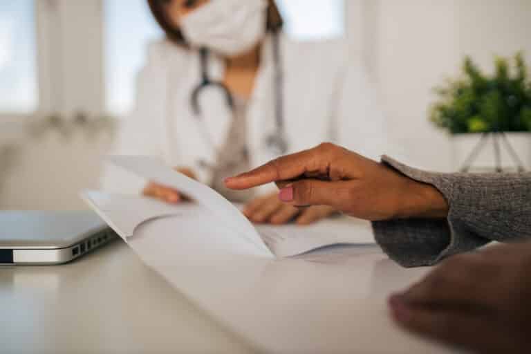 Patient pointing to a document while reviewing it with a masked doctor at a clinic desk