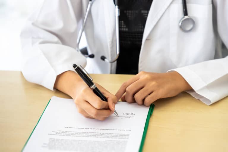 Doctor in a white coat signing a document at a desk