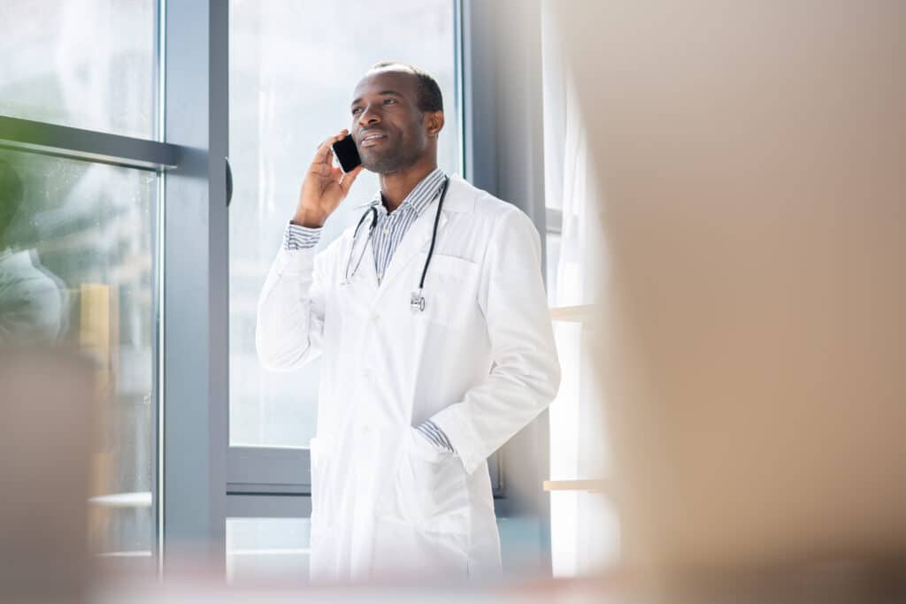 Doctor in a white coat talking on a mobile phone by a window