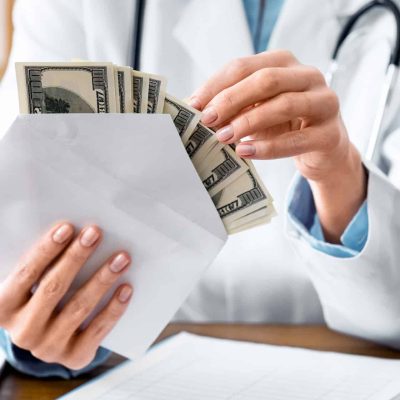 Expensive medicine. Smiling doctor counts money in envelope in interior of office, cropped