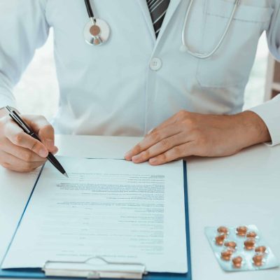Doctor hand holding pen writing patient history list on note pad and talking to the patient about medication and treatment.